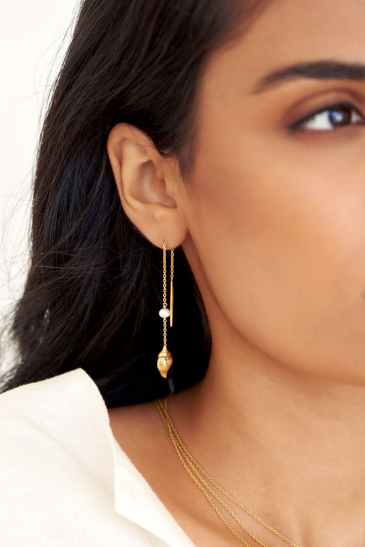 Close-up of Les Salines Gold Conch earrings featuring a white freshwater pearl, gold shell charm and delicate slide-through chain by Oceano Jewels.